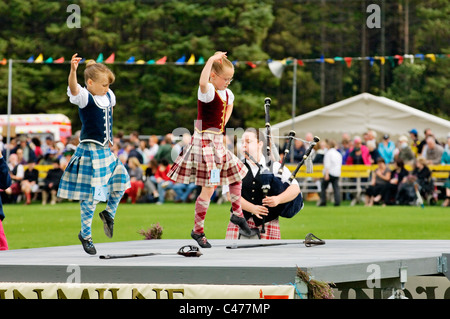 Lonach Highland Games at Strathdon, Grampian, Scotland. Piper plays for young girls performing traditional sword dance Stock Photo