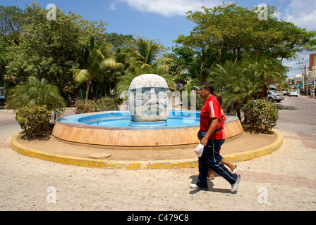 People walking past an Olmec stone head and fountain in Playa del Carmen, Riviera Maya, Quintana Roo, Mexico Stock Photo