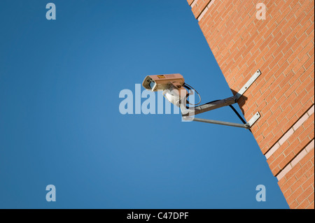 A CCTV camera attached to a brick wall on a bright and clear sky day.