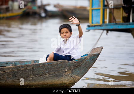 Cambodian school boy waving from wooden boat on Tonle Sap Lake in Cambodia Stock Photo