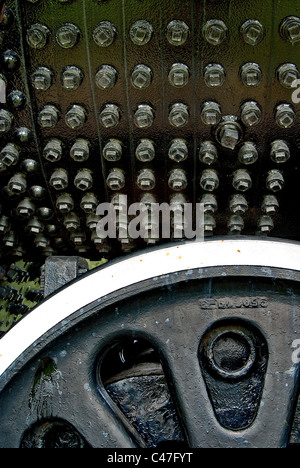 Many bolts on a black iron surface with iron wheel in foreground. Stock Photo