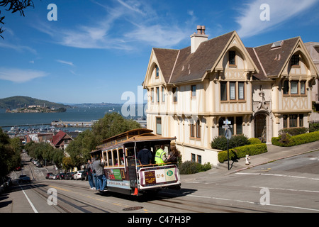 Cable car passing houses on corner of Hyde and Francisco Streets, with Alcatraz in background, San Francisco California Stock Photo