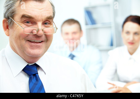 Face of senior businessman looking at camera with two partners on background Stock Photo