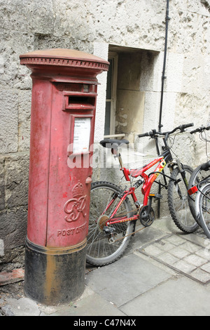 Student bicycles parked against a wall next to an old red post box in the historic university city of Oxford, England Stock Photo