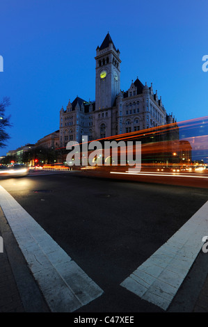 A bus speeds down Pennsylvania Avenue at twilight in front of the Old Post Office Pavilion in Washington DC. Stock Photo