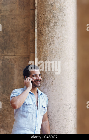 mid adult hispanic man talking on mobile phone and leaning on columns outdoors. Verticl shape, side view, copy space Stock Photo