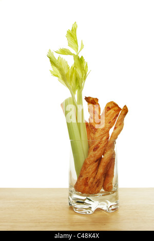 Cheese twists and celery in a glass on a wooden board against a white background Stock Photo