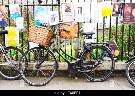 retro bicycle chained to metal rail fence in a cambridge city centre, surrounded by notices and posters Stock Photo