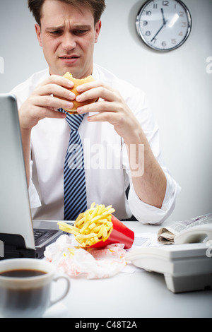 Portrait of disgusted businessman eating hamburger during lunch break Stock Photo