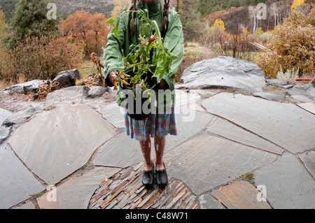 A girl waters a tomato plant in the rain on a flagstone patio outside  her Colorado home in the fall. Stock Photo