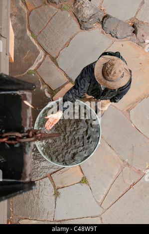 View from above of a woman standing by a rain catchment barrel, holding her hand out. Stock Photo