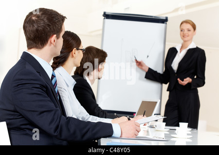 Photo of serious business people listening to female manager pointing at whiteboard while presenting new project Stock Photo