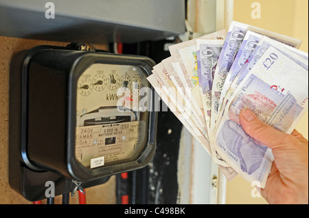 Woman holding cash in front of electric meter after learning of energy price rises in the UK Stock Photo