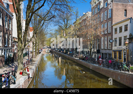 Two young women sitting by Oudezijds Achterburgwal canal in the Red Light District (De Wallen) in Spring, Amsterdam, Netherlands Stock Photo