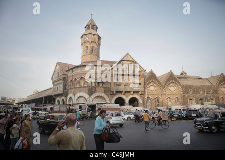People walk along a crowded street in india with an ornate building in the background. Stock Photo