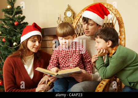 Little boy surrounded by his family members trying to read book Stock Photo