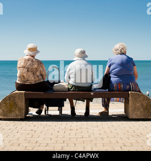 a rear view of three old elderly women sitting on a seaside bench Aberystwyth Wales UK Stock Photo