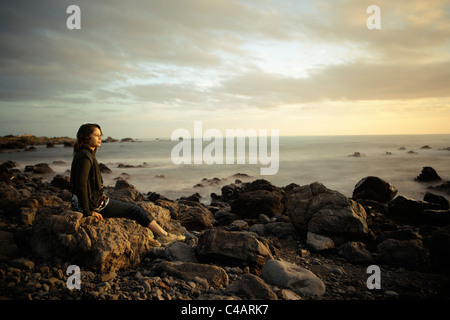 Woman, sunset, rocky shore, New Zealand. Combined long exposure. Stock Photo
