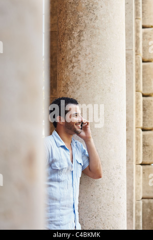 mid adult hispanic man talking on mobile phone and leaning on columns outdoors. Verticl shape, side view, copy space Stock Photo