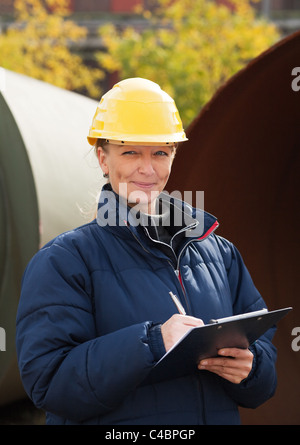 Woman in yellow hard hat taking notes while standing in a construction site Stock Photo