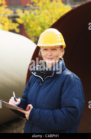 Female engineer in yellow hard hat taking notes at construction site Stock Photo