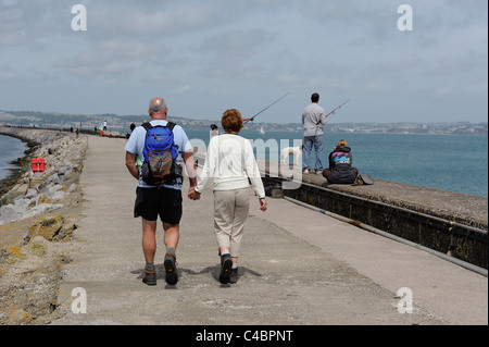 A couple walking along brixham breakwater alongside people fishing devon england uk Stock Photo