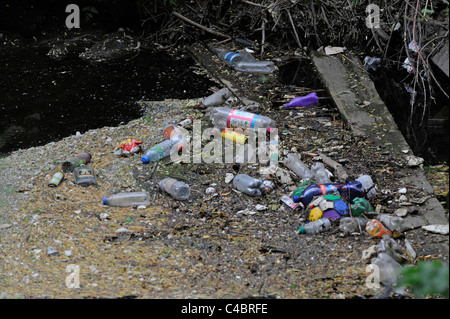 Discarded plastic bottles and other rubbish lay on top of a slow running river or stream. Stock Photo