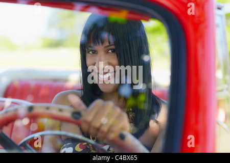 young adult brunette woman driving convertible red car and looking at camera. Horizontal shape, front view