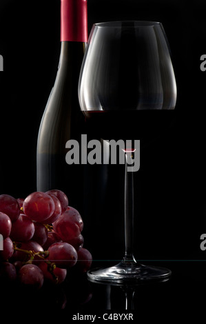 Glass of red wine on black background with bunch of grapes
