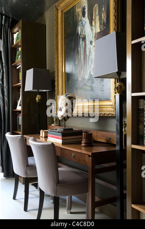 Gilt framed oil painting above wooden writing desk with mounted African mask and upholstered chairs Stock Photo