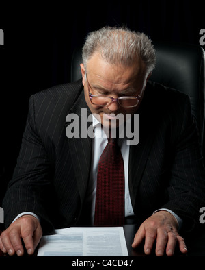 The elderly man in eyeglases reads the document. A photo against a dark background Stock Photo