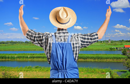 A farmer gesturing with raised hands with field in the background Stock Photo