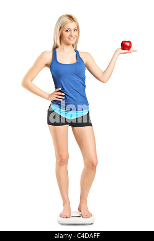 Full length portrait of a smiling woman holding a red apple and standing on a weight scale Stock Photo