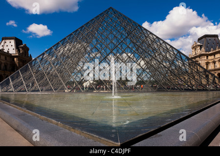 Glass Pyramid and fountain entrance to the Louvre museum Paris France beautiful Blue sky background and dimensional clouds Stock Photo