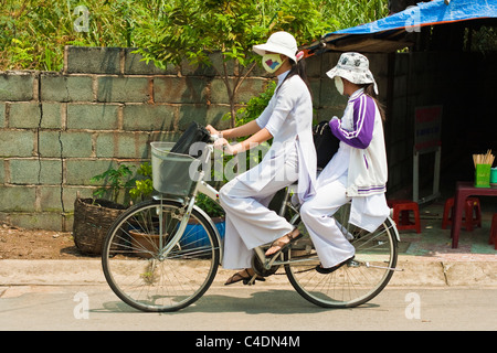 Two students in Ao Dai dress cycle home from school Stock Photo