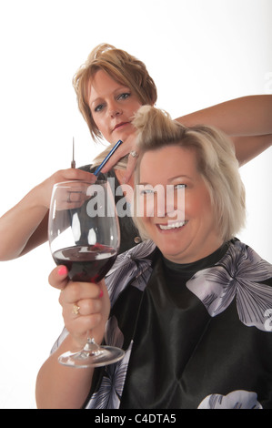 Hair stylist working on female customer with glass of red wine Stock Photo