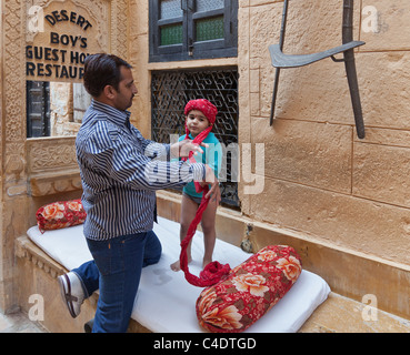 Indian father preparing a turban for his young son to wear in a street in Jaisalmer, Rajasthan India Stock Photo