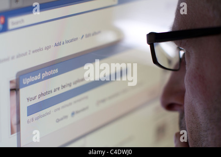 Male uploading photos to Facebook, Facebook now employs face recognition software Stock Photo