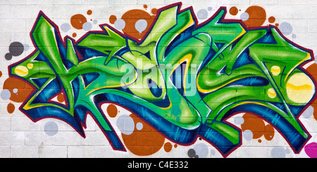 A colorful green, blue, and orange graffiti painting on a white brick wall Stock Photo