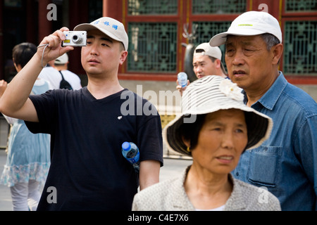 Chinese middle class tourist / tourists with baseball caps / sun hat taking a photo / photograph in The Summer Palace in Beijing, China. Stock Photo