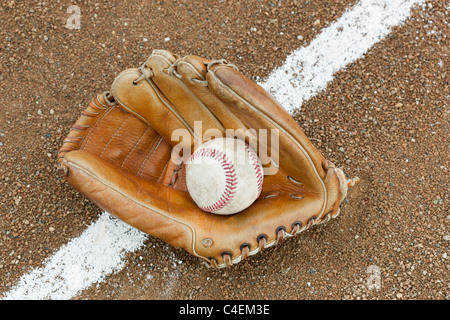An old worn baseball glove with a ball on a baseball field Stock Photo