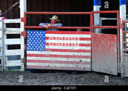 Rodeo official stands behind mud spattered gate. Stock Photo