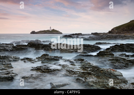 Waves crash over the rocks of Godrevy Point at sunset, looking towards Godrevy Lighthouse, Cornwall, England. Stock Photo