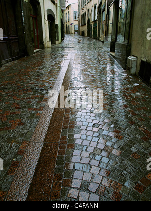 Rain-soaked cobblestone street in a quaint European town captured during early morning hours Stock Photo