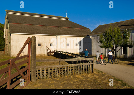 Family walking with bicycles past farm barns at Wilder Ranch State Park, Santa Cruz, California Stock Photo