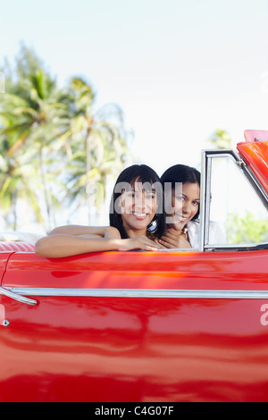 young adult brunette twin women driving convertible red car and looking at camera. Vertical shape, side view, copy space Stock Photo