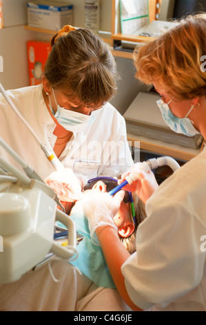 Female dentist and assistant working together on patient in dental chair Stock Photo