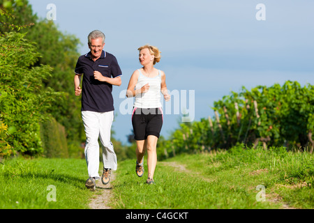 Mature or senior couple doing sport outdoors, jogging down a path in summer Stock Photo