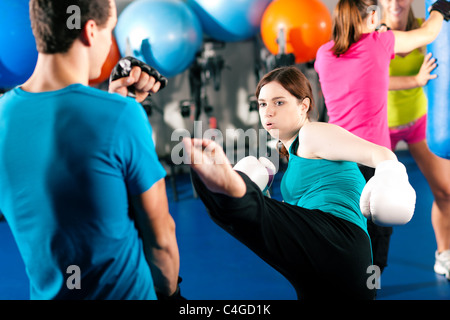 Woman Kick boxer kicking her trainer in a sparring session, in the background other boxers are hitting the sandbag Stock Photo