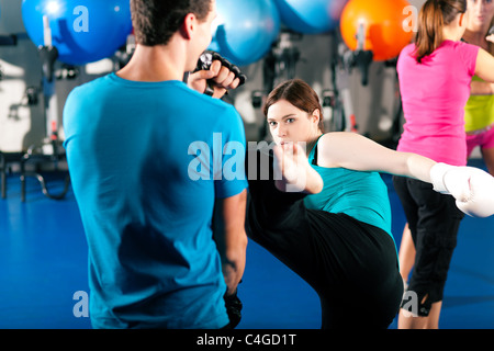 Woman Kick boxer kicking her trainer in a sparring session, in the background other boxers are hitting the sandbag Stock Photo